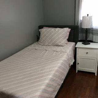 A minimalist bedroom with a single bed and a nightstand featuring a lamp.