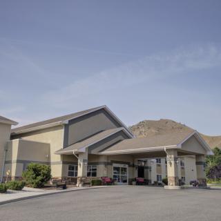 A modern building with a driveway and mountain in the background on a clear day.