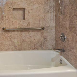 A bathroom featuring a bathtub with tiled walls and a grab bar.