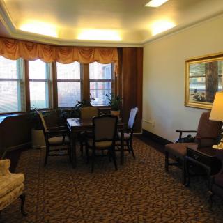 A cozy living room with a table and chairs set, surrounded by large windows and warm lighting.