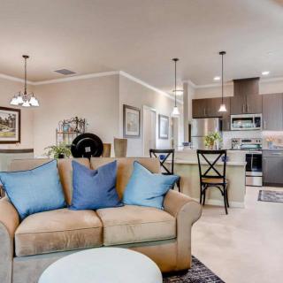 A modern open-concept living area with a comfortable sofa featuring blue pillows, a kitchen island with barstools, and elegant pendant lighting.
