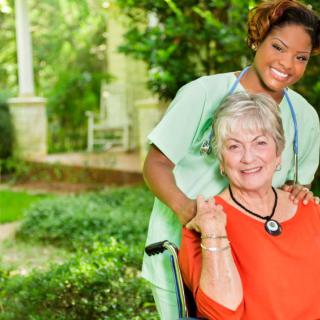 A caregiver and an elderly woman smiling together in a garden.