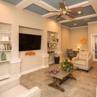 A cozy living room featuring a ceiling fan, built-in bookshelves, a large television, and comfortable seating.