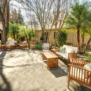 A serene outdoor patio with wooden furniture surrounded by lush greenery and sunlight.