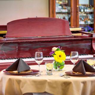A beautifully set dining table with a piano in the background, featuring elegant dishware and a vibrant floral centerpiece.