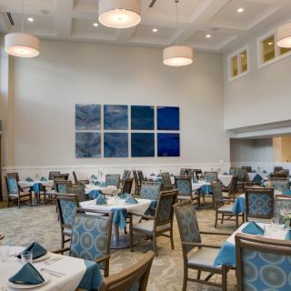 A modern restaurant dining area with neatly arranged tables and chairs, featuring elegant decor and artwork on the wall.