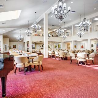 An elegant dining room with plush carpet, chandeliers, and a grand piano.