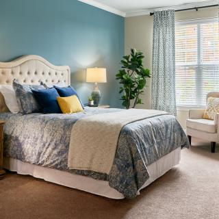 A cozy and modern bedroom with a neatly made bed, accent pillows, and a stylish lamp beside an armchair.
