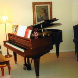 A cozy living room featuring a grand piano with sheet music on its stand, surrounded by warm lighting and artwork.