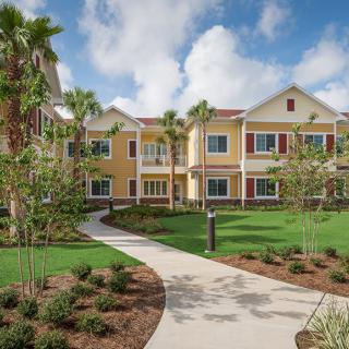 A sunny residential complex with palm trees and a well-maintained lawn.