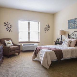 A cozy bedroom with a single bed, armchair, and decorative elements surrounding a bright window.