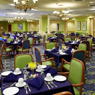 A spacious dining room with neatly arranged tables and chairs, featuring elegant place settings and chandeliers.