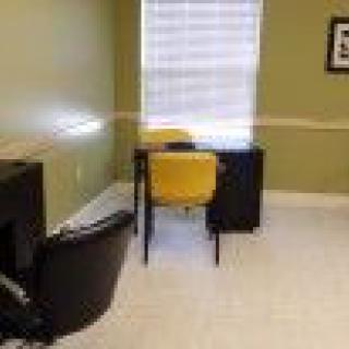 A simple office setup with a desk and chairs near a window.
