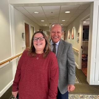 Two friends posing together in a hallway, both smiling warmly.