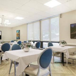 A neatly arranged dining area with tables and blue-cushioned chairs, decorated with potted plants and artwork on the walls.