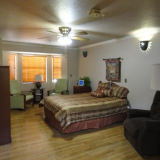 A cozy and well-furnished bedroom featuring a comfortable bed, chairs, and natural light from the windows.