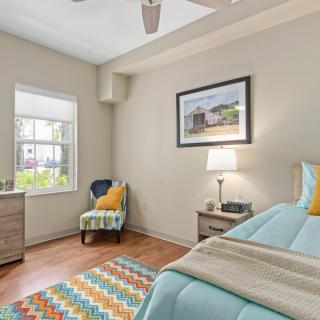 A cozy bedroom with modern decor, featuring a neatly made bed, a colorful rug, and natural light from the window.