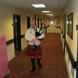 A person playing bagpipes while walking down a hallway in traditional clothing.