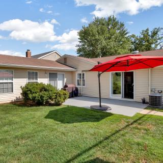 A sunny backyard featuring a patio with a red umbrella and well-maintained lawn.