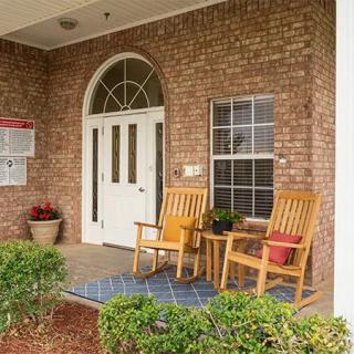 A cozy porch with wooden chairs and potted plants at the entrance of a brick house.