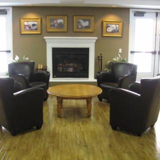A cozy living room with a fireplace, surrounded by leather armchairs and a wooden table.
