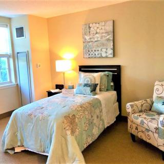 A cozy bedroom with a single bed, patterned armchair, and warm lighting.