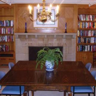 A cozy library room with bookshelves, a fireplace, and a central table with chairs.