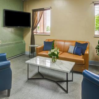 A cozy living room with a leather sofa, blue chairs, and a marble coffee table facing a wall-mounted television.