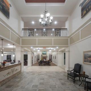 A spacious and well-lit lobby with a central chandelier, reception desk, and seating area.