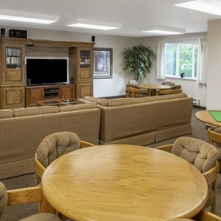 A cozy living room with a large sofa, entertainment center, and round wooden table with chairs.