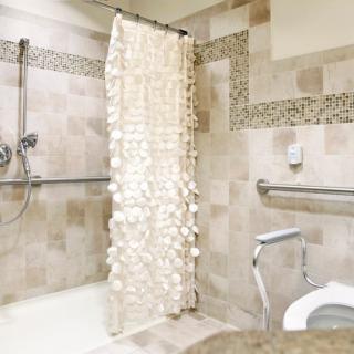 An accessible bathroom with tiled walls, a shower area with handrails, and a decorative shower curtain.
