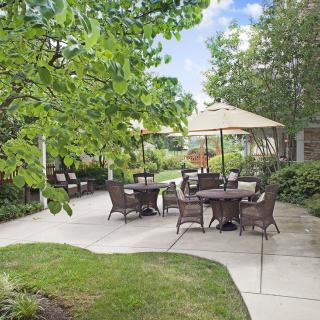 A serene outdoor patio area with tables and chairs, shaded by large umbrellas and surrounded by lush greenery.