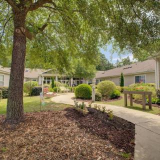 A peaceful garden setting with a pathway leading to a building surrounded by trees and bushes.