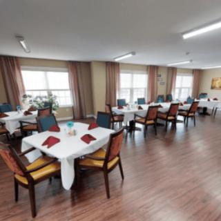 A well-arranged dining room with tables set for guests, featuring large windows and hardwood flooring.