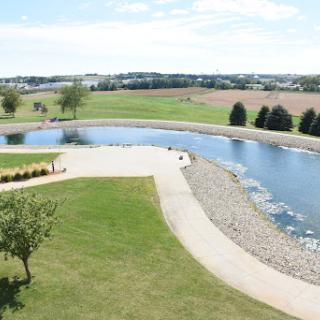 A serene view of a park with a winding river, lush green lawns, and trees under a bright sky.