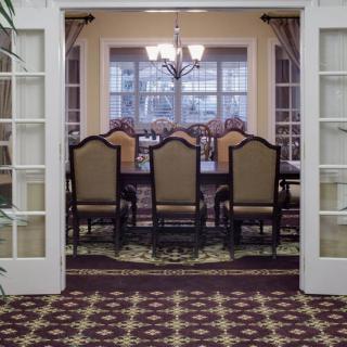 A dining room with a set of chairs around a long table, illuminated by a chandelier, viewed through open French doors.