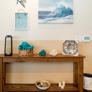 A beach-themed interior setting with a wooden table adorned with nautical decorations, including a sea wave painting and various ornaments.