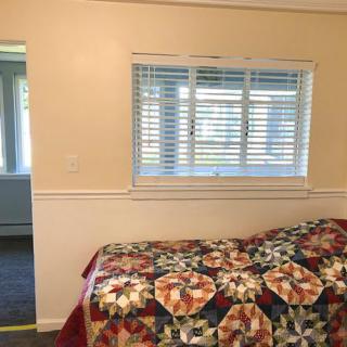A cozy bedroom with a colorful quilt on the bed and sunlight streaming through the window blinds.
