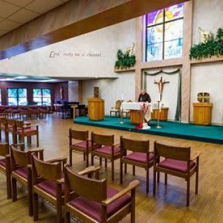 Interior of a chapel with an altar, cross, and chairs arranged for a service.