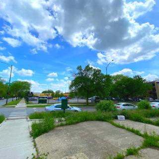 A scenic view of an urban area featuring a cloudy sky and overgrown greenery alongside a sidewalk.