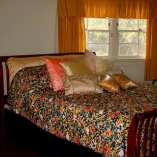 A cozy bedroom with a colorful quilt, multiple pillows, and yellow curtains.