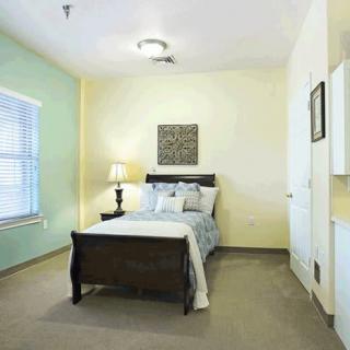 A cozy bedroom with a bed, lamp, and window, featuring soft lighting and simple decor.