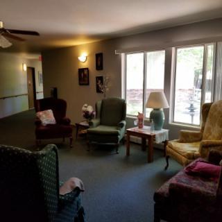 A cozy living room with multiple chairs arranged around a central table near a large window.