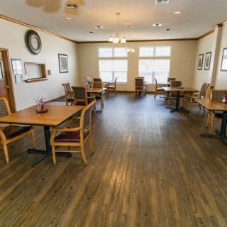 A spacious dining room featuring wooden floors, multiple tables and chairs, and large windows allowing natural light to fill the space.