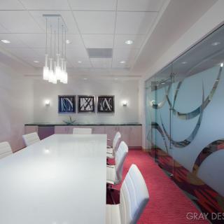 A modern conference room featuring a large white table and chairs, abstract artwork, and a decorative glass partition.