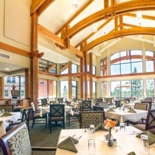 A spacious and elegantly designed restaurant interior with large windows and wooden beams, filled with natural light.