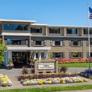 A well-maintained building with colorful flowerbeds and an American flag on a sunny day.
