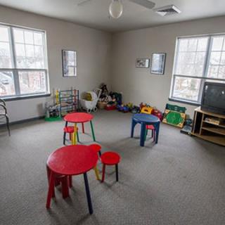 A children's playroom with colorful tables, chairs, toys, and a TV.