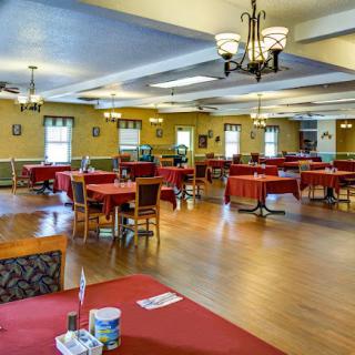 An empty dining hall with red tablecloths and chandeliers.