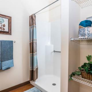 A well-organized bathroom featuring a shower with a patterned curtain, neatly folded towels, and decorative elements on shelves.